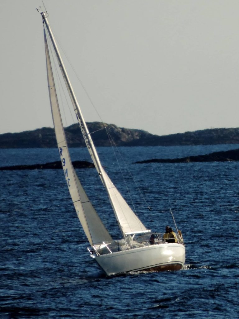 Zeilboot op donkerblauw water voor een heuvelrug